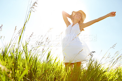 Buy stock photo A carefree young woman standing with her arms outstretched in a meadow while smiling blissfully