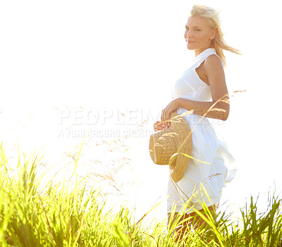 Buy stock photo Side view of a gorgeous young woman standing in a meadow holding her sunhat - portrait