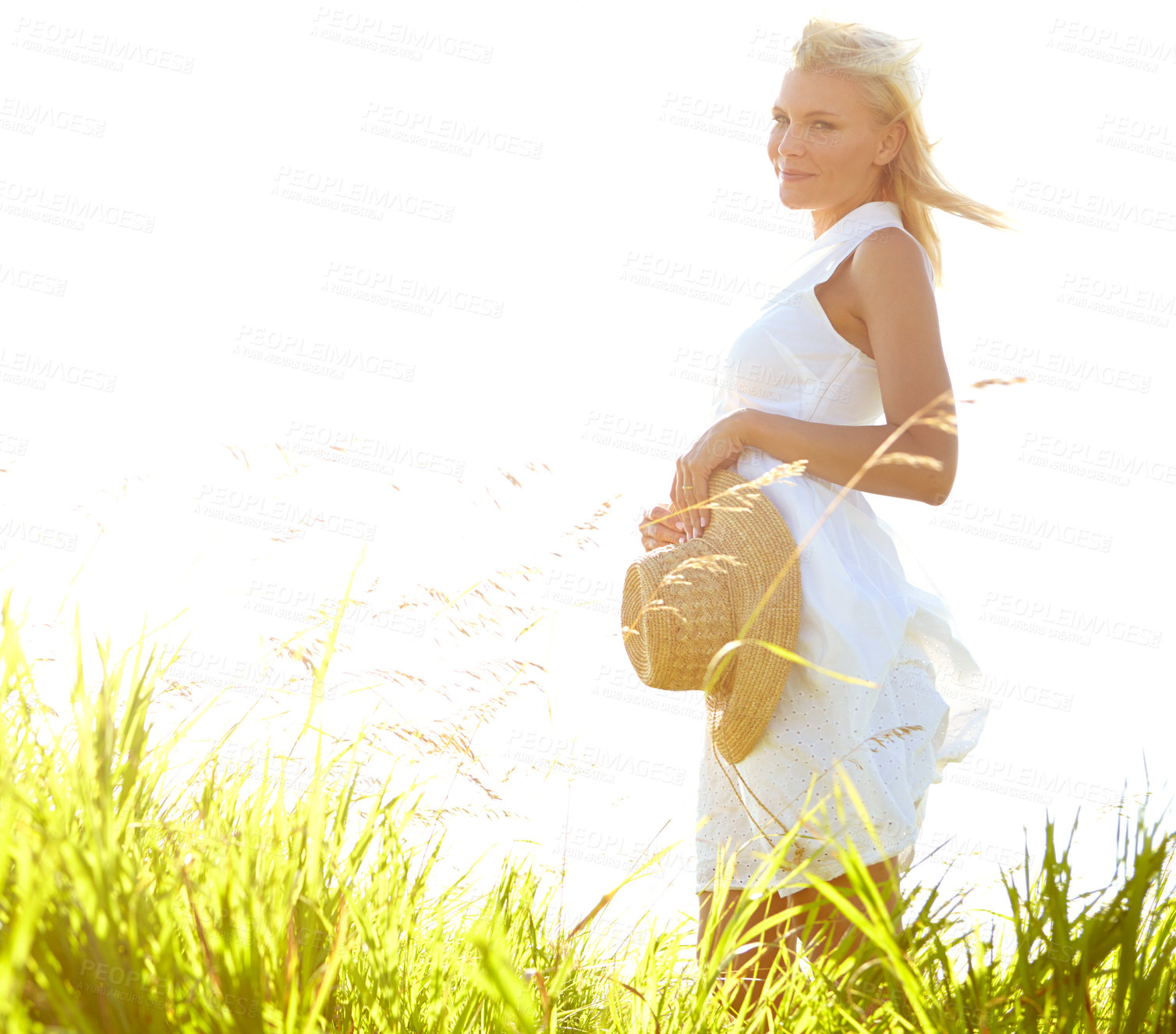 Buy stock photo Side view of a gorgeous young woman standing in a meadow holding her sunhat - portrait