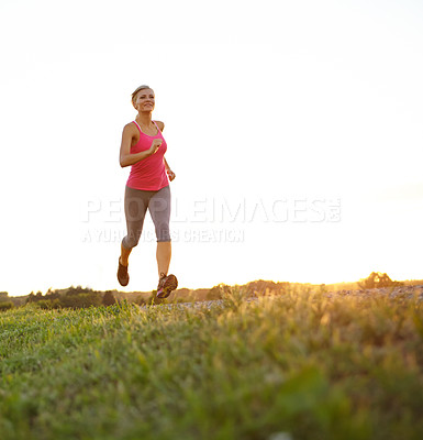 Buy stock photo A beautiful young woman jogging as the sun sets behind her