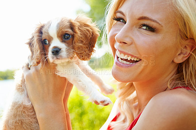 Buy stock photo Portrait of a happy beautiful blonde holding up an adorable puppy in the outdoors