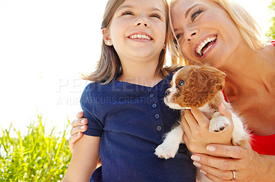 Buy stock photo Shot of a little girl holding a puppy while her mother smiles at her lovingly 