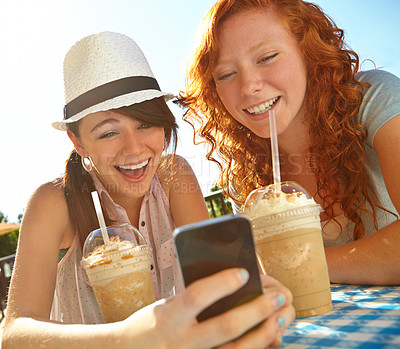 Buy stock photo Two adolescent girls enjoying smoothies while texting on a cellphone