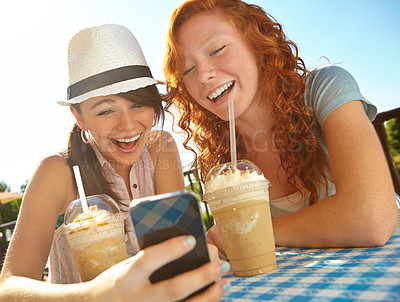 Buy stock photo Two adolescent girls enjoying smoothies while texting on a cellphone