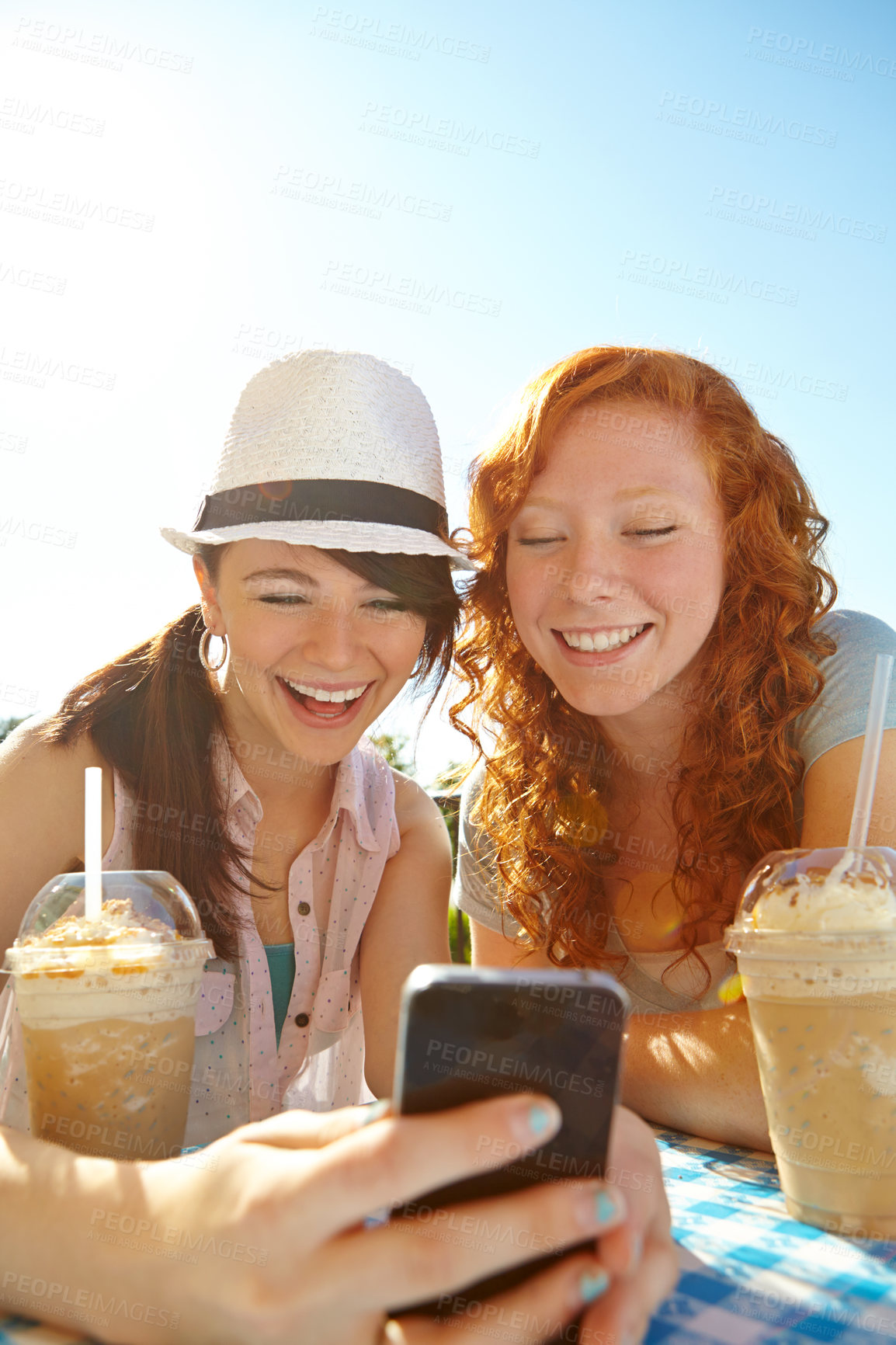 Buy stock photo Two adolescent girls enjoying smoothies while texting on a cellphone