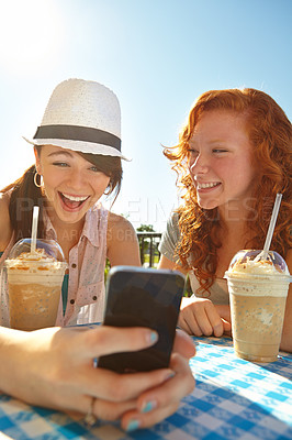 Buy stock photo Two adolescent girls enjoying smoothies while texting on a cellphone