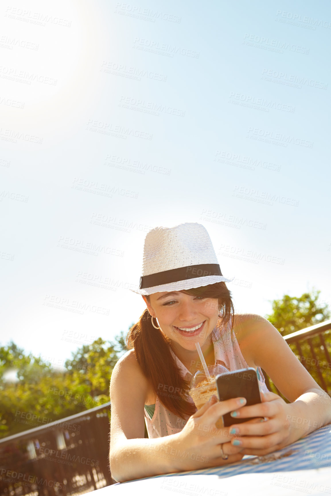 Buy stock photo A happy teenage girl texting on a smartphone while enjoying a smoothie at an outdoor cafe