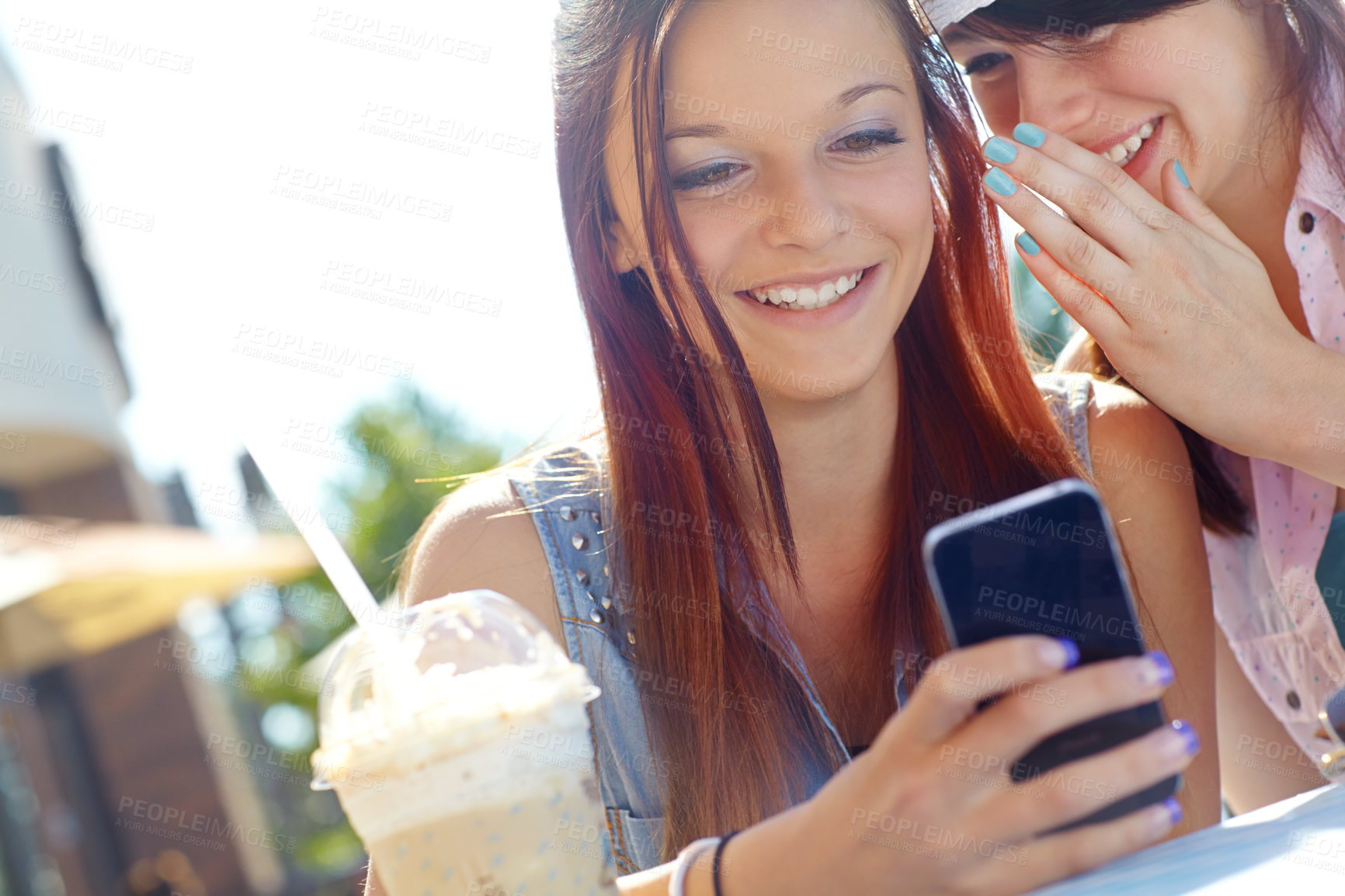 Buy stock photo A teenage girl texting on a cellphone while her friend whispers something in her ear