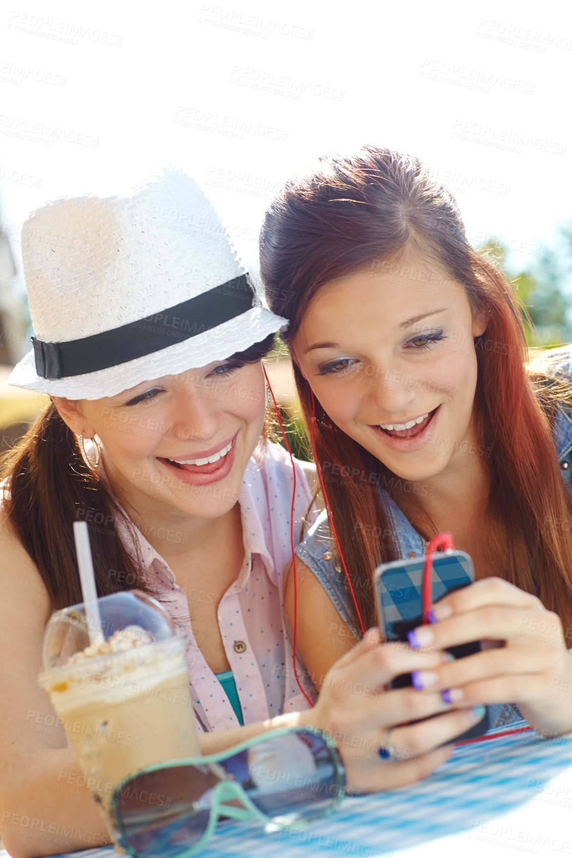 Buy stock photo Two adolescent girls sharing earphones while listening to music on a mobile phone