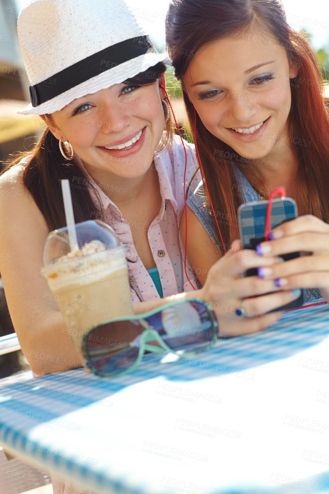 Buy stock photo Music, phone and smile of woman at cafe, drinking ice coffee outdoor in park together for break. App, social media and streaming with girls on blanket in nature for bonding or communication