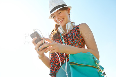 Buy stock photo A happy teenage girl smiling while holding a smartphone with her headphones attached to it