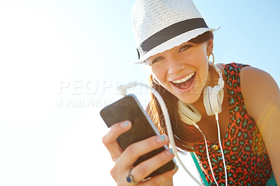 Buy stock photo A happy teenage girl smiling while holding a smartphone with her headphones attached to it