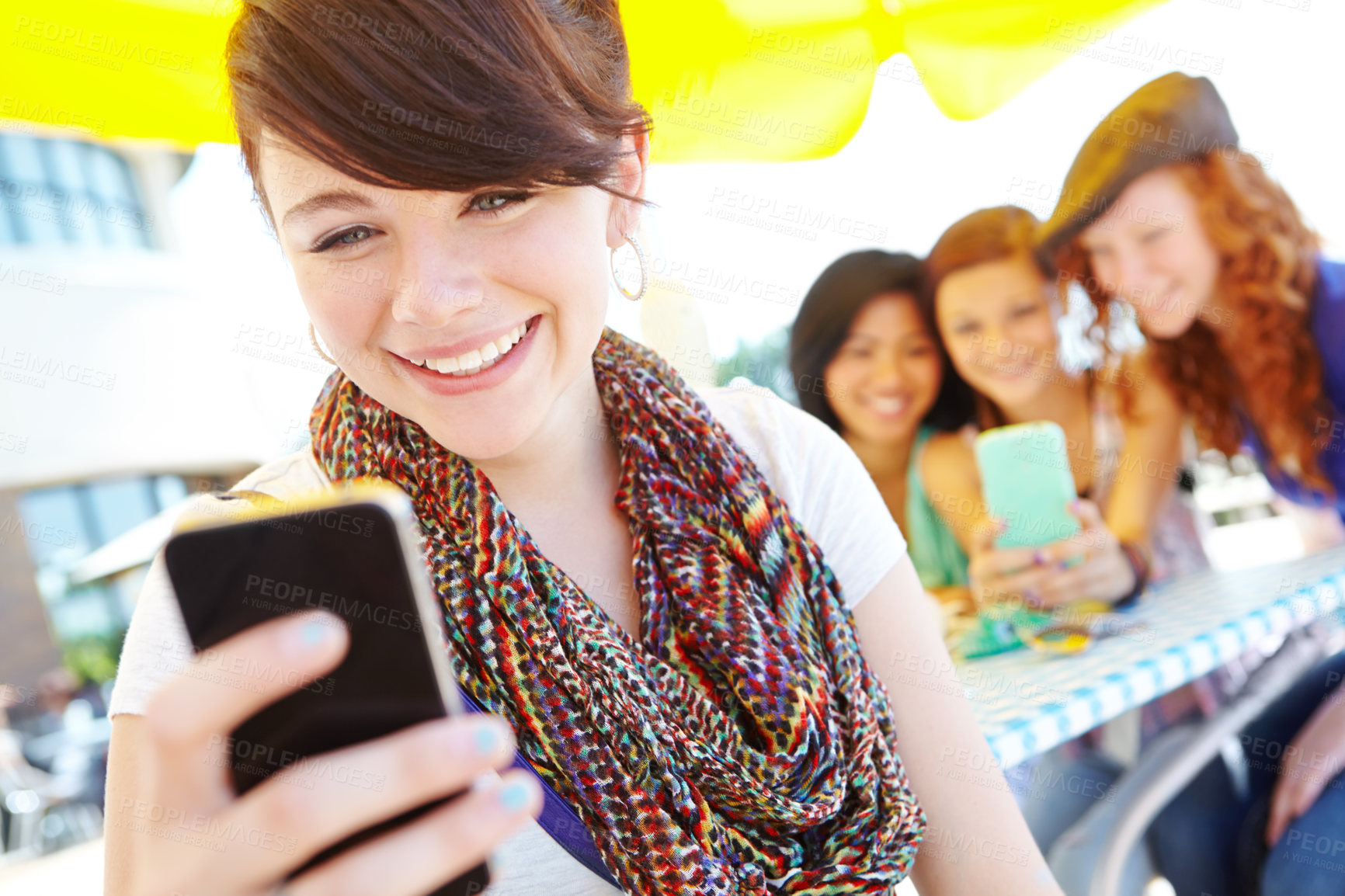 Buy stock photo A beautiful young adolescent girl holding a cellphone with her friends in the background