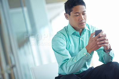 Buy stock photo A professional asian businessman sending a text message with his smartphone