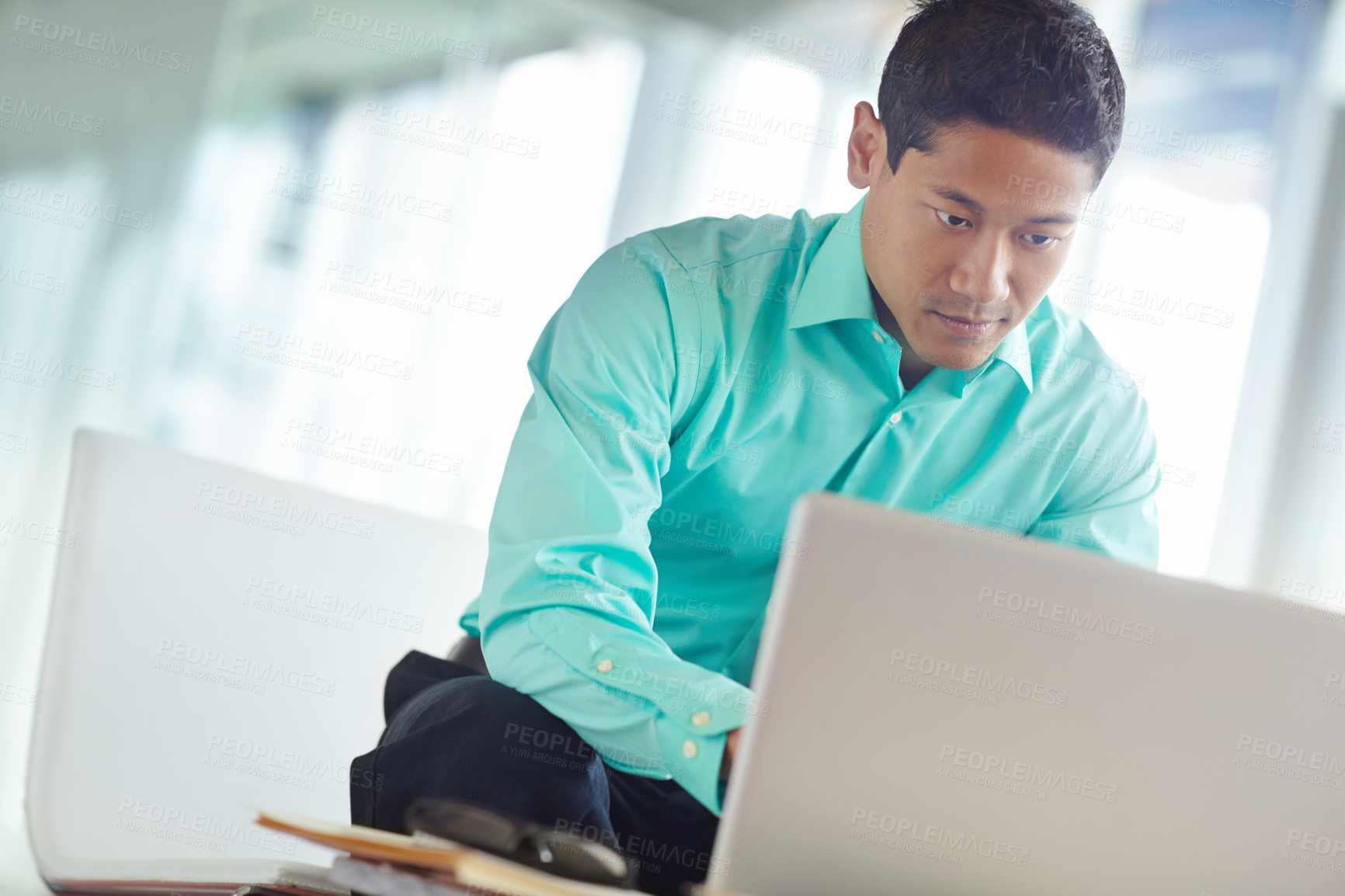 Buy stock photo Handsome young asian businessman using his laptop while at work