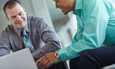 Buy stock photo Two handsome young businessmen working together while sharing a laptop between them