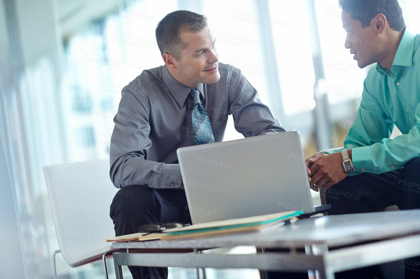 Buy stock photo Two handsome young businessmen working together while sharing a laptop between them