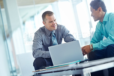 Buy stock photo Two handsome young businessmen working together while sharing a laptop between them