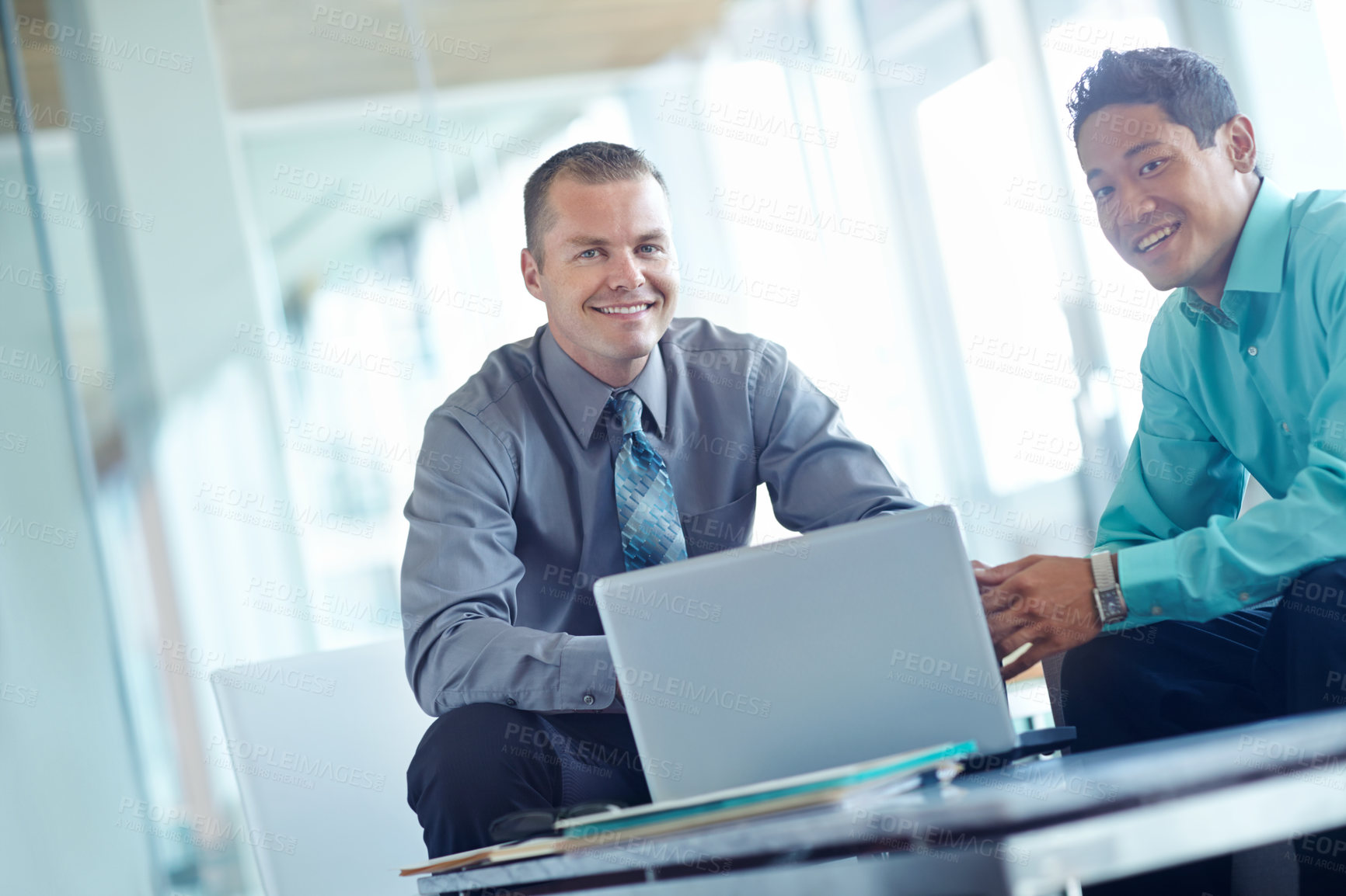 Buy stock photo Two handsome young businessmen working together while sharing a laptop between them