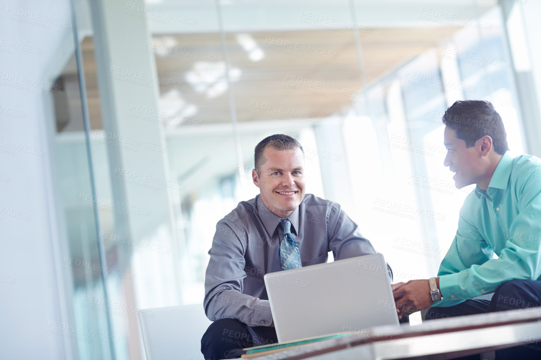 Buy stock photo Two handsome young businessmen working together while sharing a laptop between them