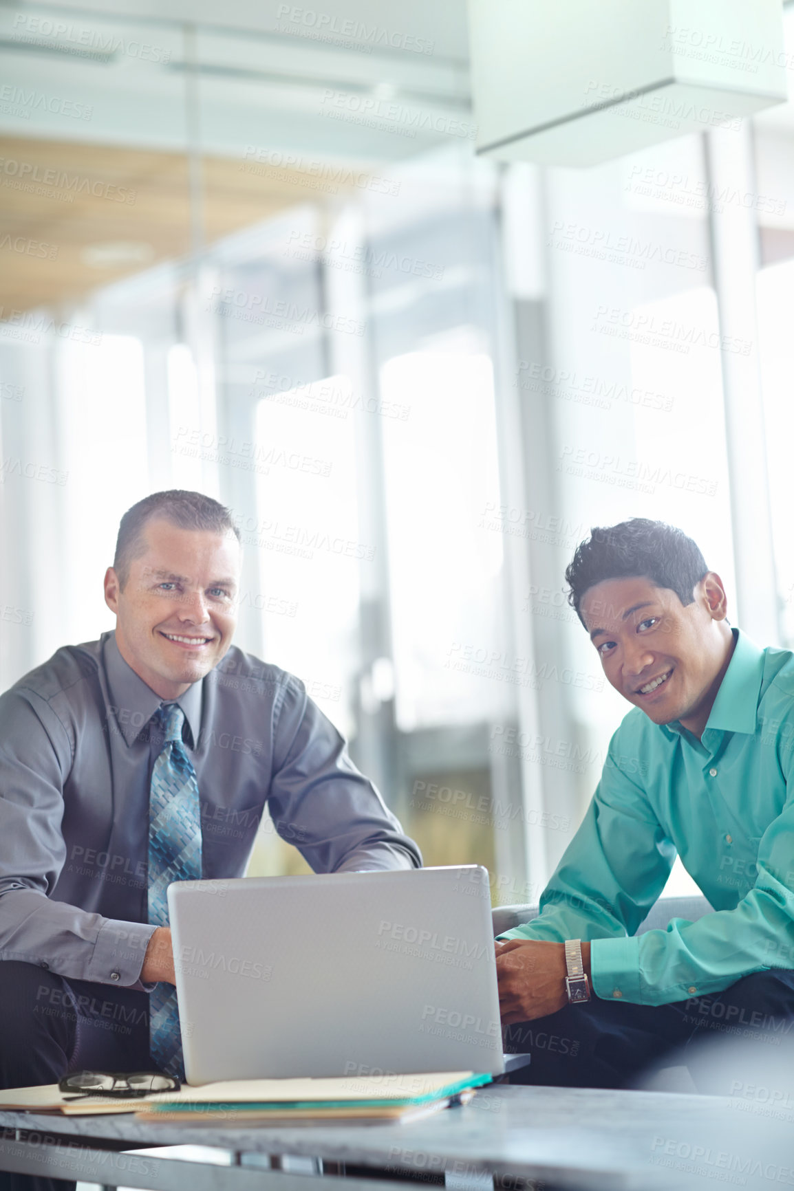 Buy stock photo Two handsome young businessmen working together while sharing a laptop between them