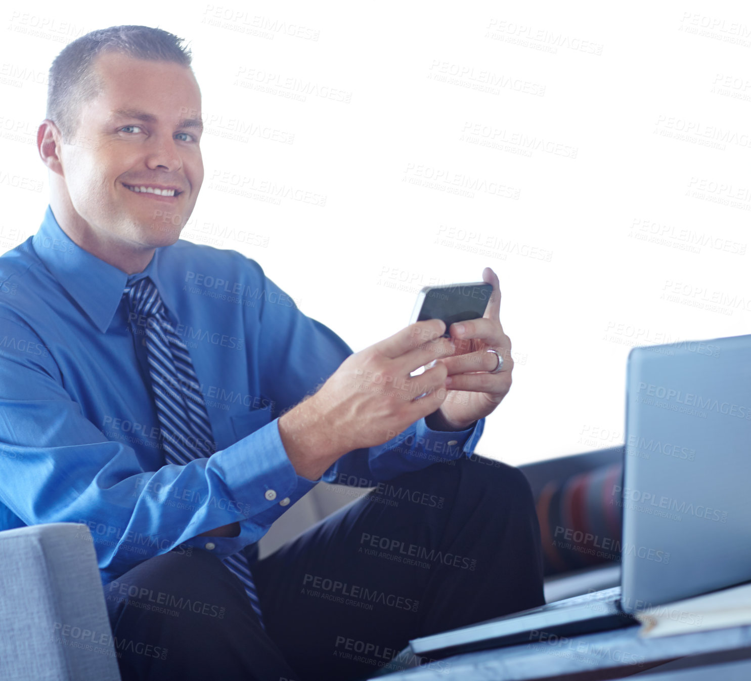 Buy stock photo A young caucasian businessman using his smartphone with his laptop before him as he works