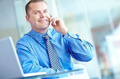 Buy stock photo A young caucasian businessman using his smartphone with his laptop before him as he works