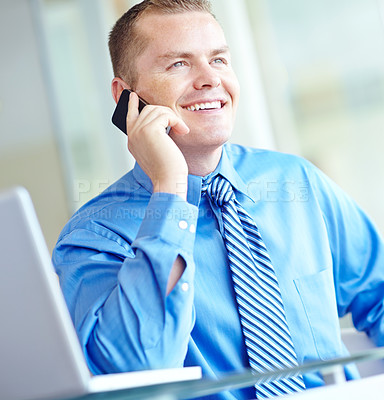 Buy stock photo A young caucasian businessman using his smartphone with his laptop before him as he works