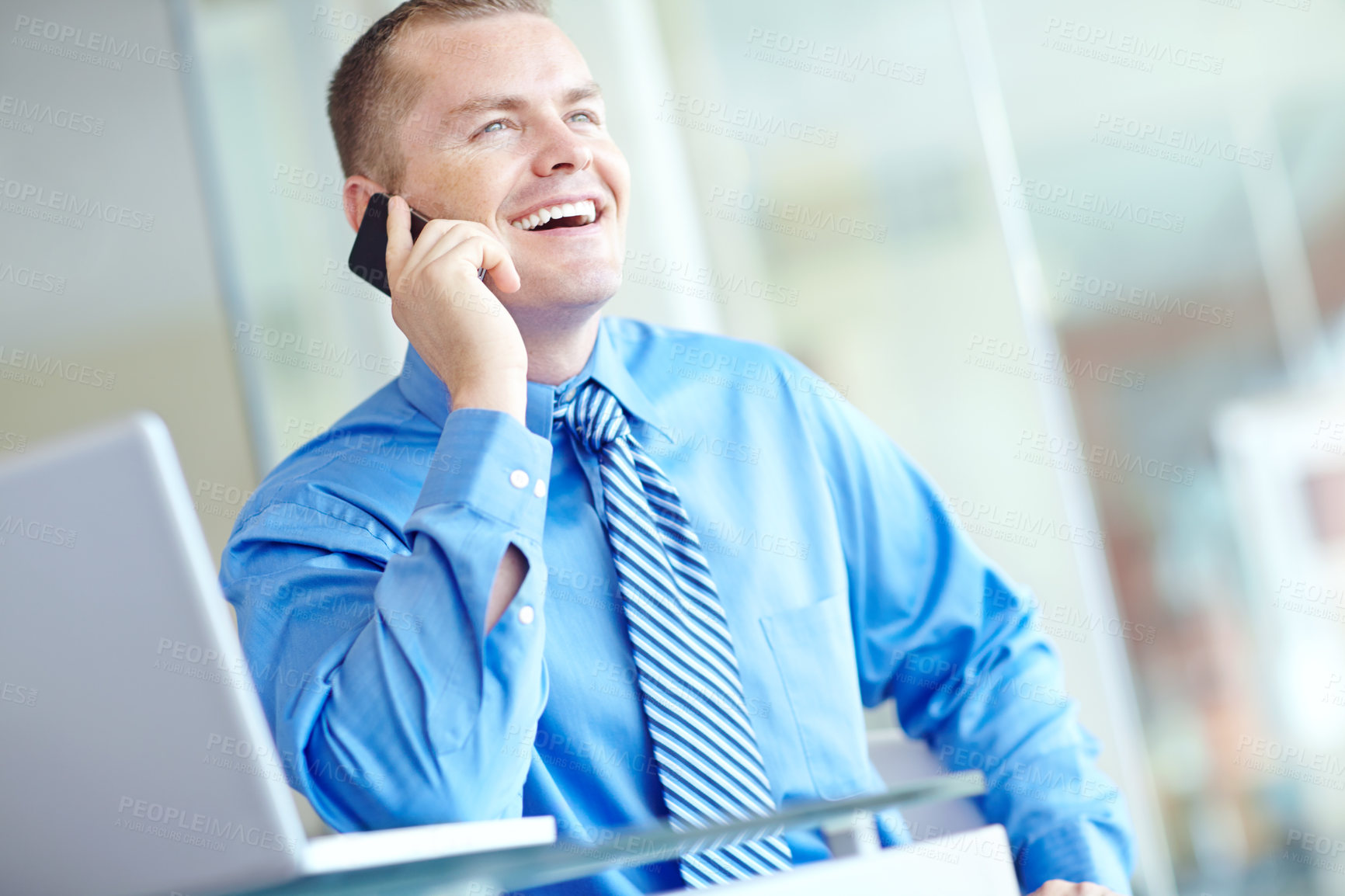 Buy stock photo A young caucasian businessman using his smartphone with his laptop before him as he works