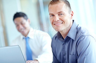 Buy stock photo Smiling caucasian businessman with an asian coworker working in the background