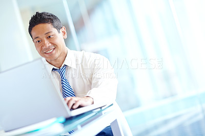 Buy stock photo A smiling asian businessman using his laptop while working