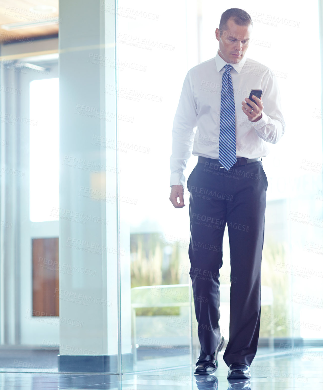 Buy stock photo A serious caucasian businessman using his smartphone while working