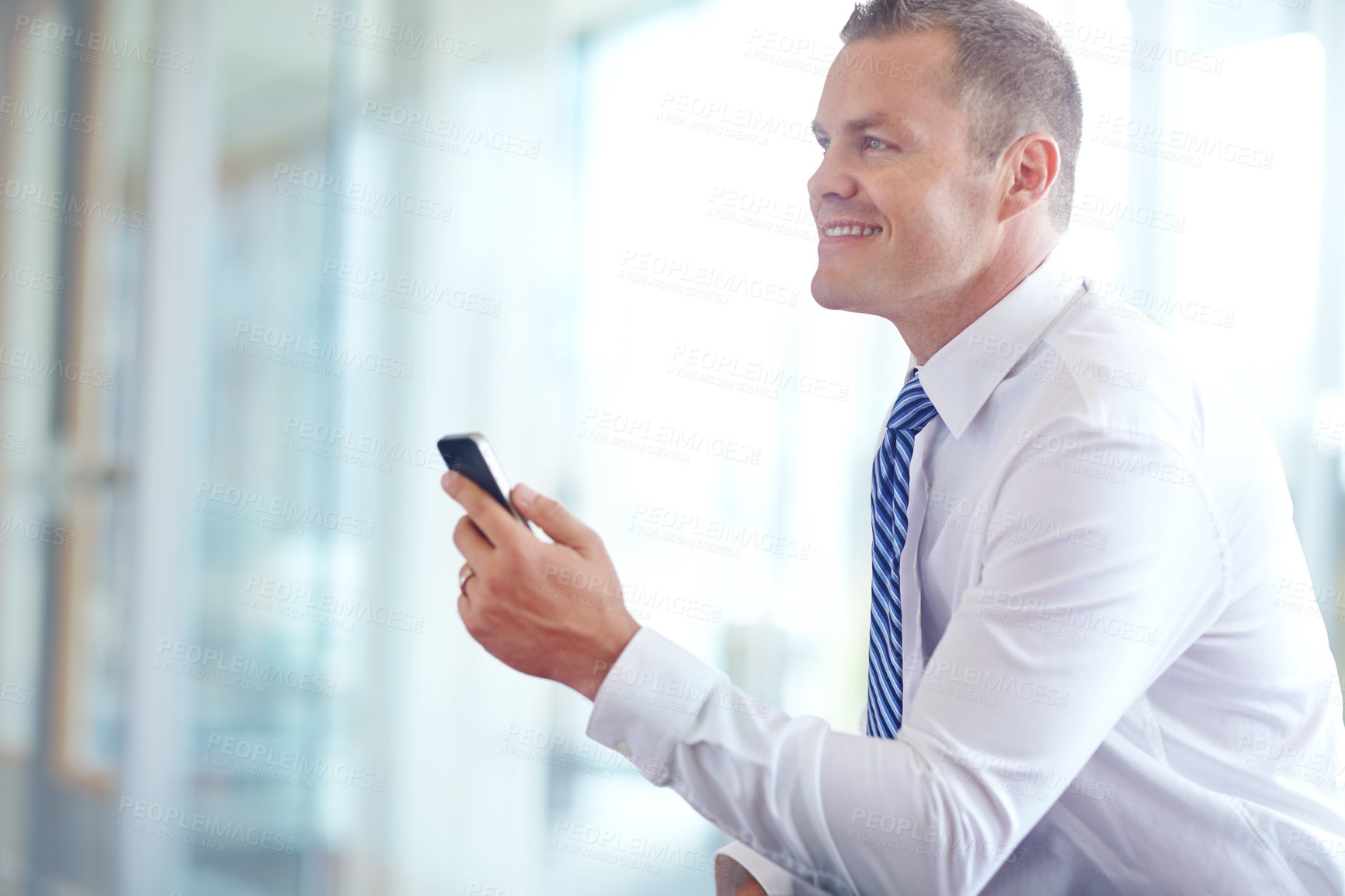 Buy stock photo A smiling caucasian businessman using a smartphone wile working