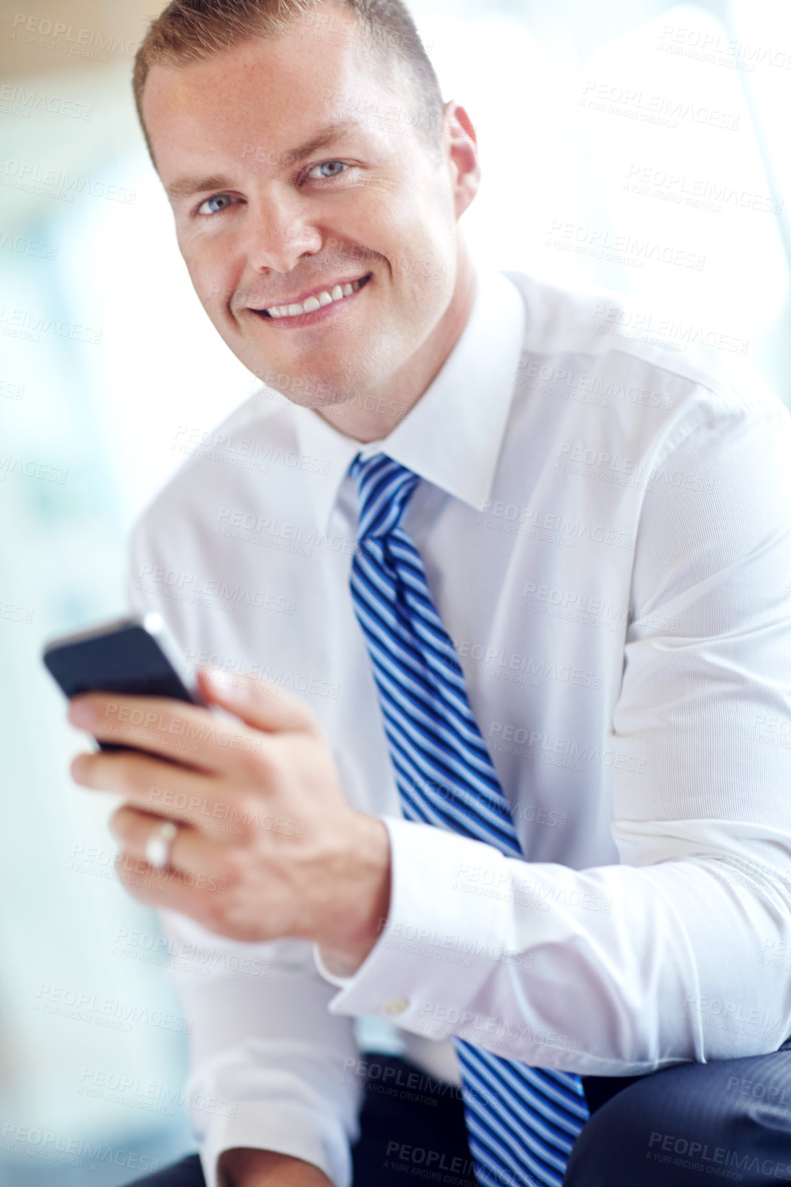 Buy stock photo A smiling caucasian businessman using a smartphone wile working