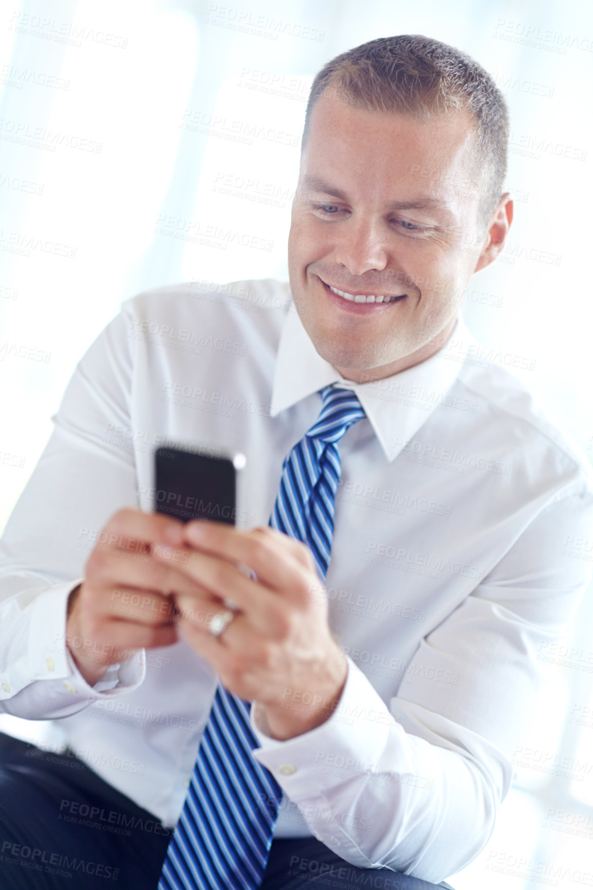 Buy stock photo A smiling caucasian businessman using a smartphone wile working