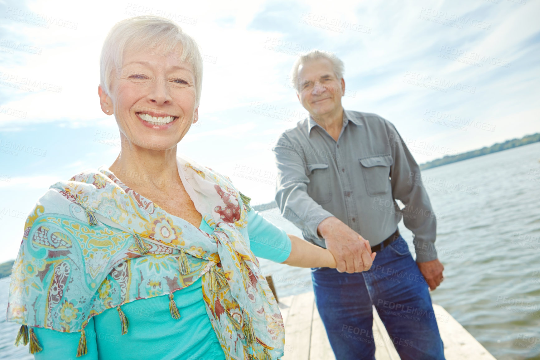 Buy stock photo An attractive elderly woman holding her husband's hand and leading him along the pier