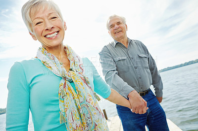 Buy stock photo Portrait, elderly couple and holding hands at lake for love, support and relationship on holiday. Retirement, man and woman together by water jetty for travel, smile and loyalty to partner outdoor