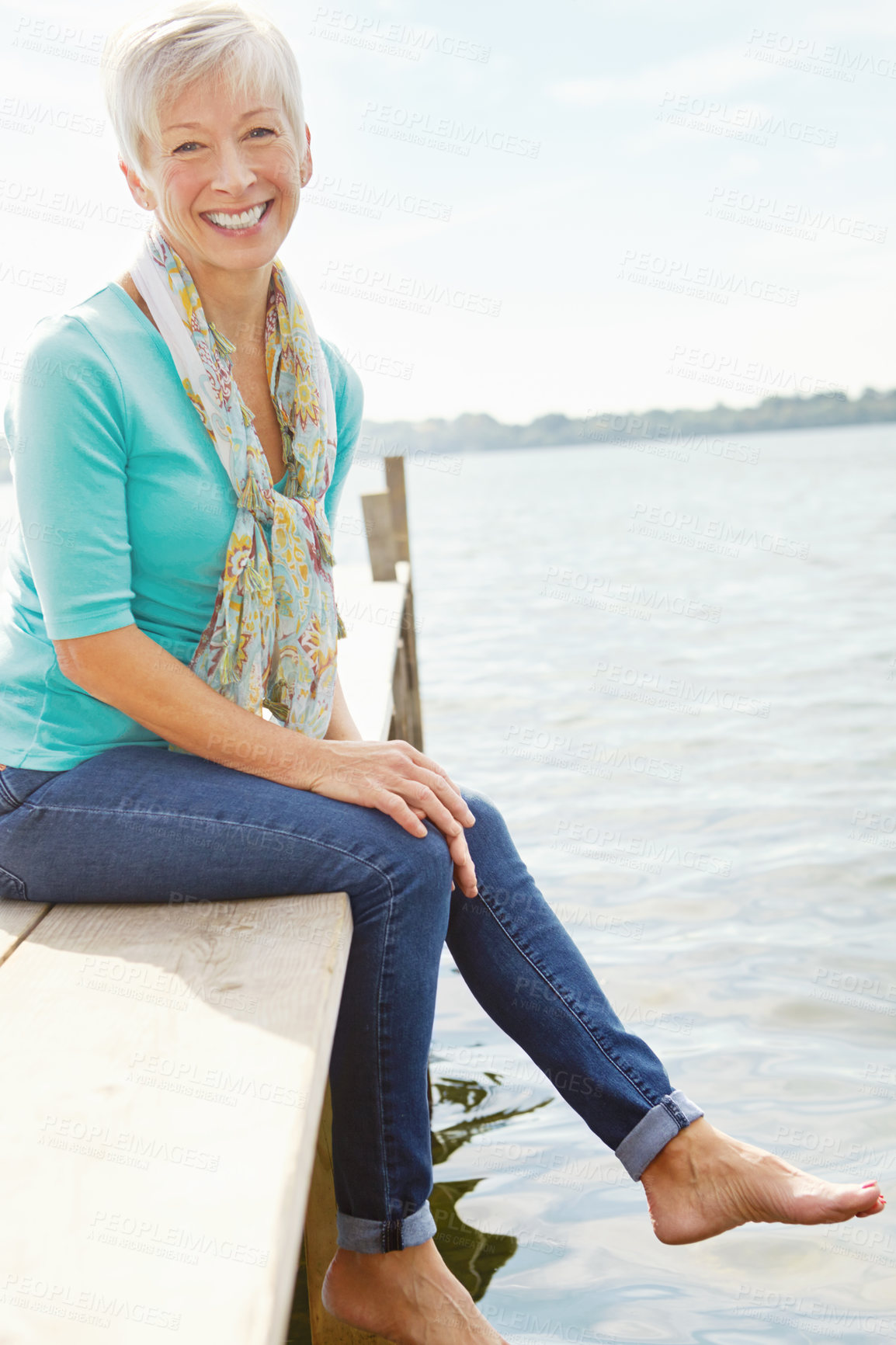 Buy stock photo Image of a mature woman sitting on a jetty and splashing her feet in the water