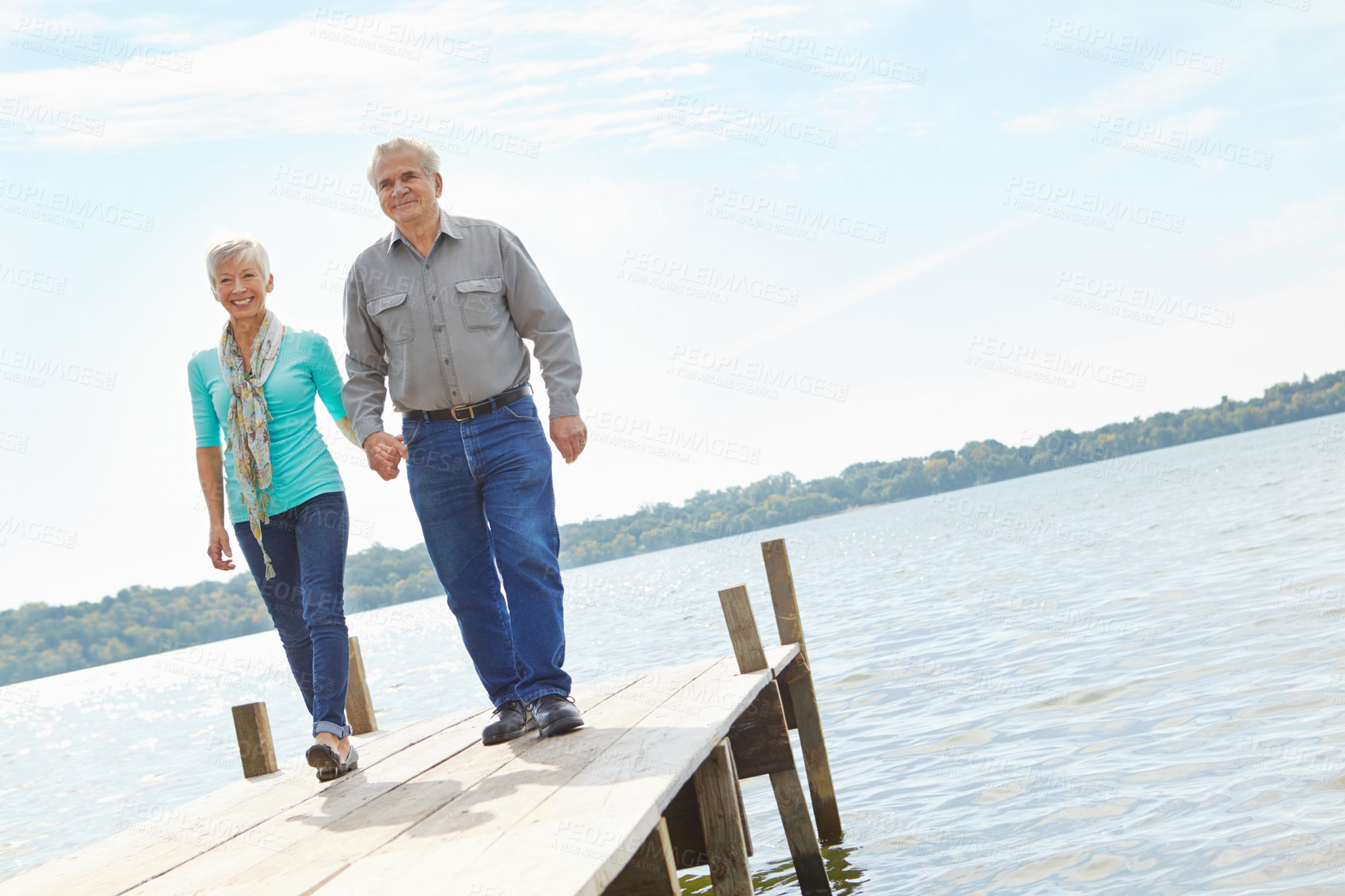 Buy stock photo Happy, elderly and couple walking on pier for retirement, vacation journey and travel destination. Below, senior people and holding hands for marriage commitment, holiday location and bonding on lake