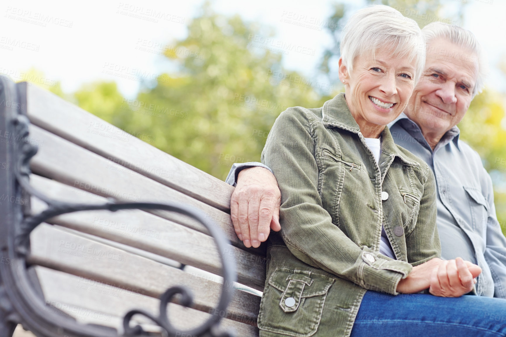 Buy stock photo Portrait of a mature couple sitting on a bench together and smiling at the camera