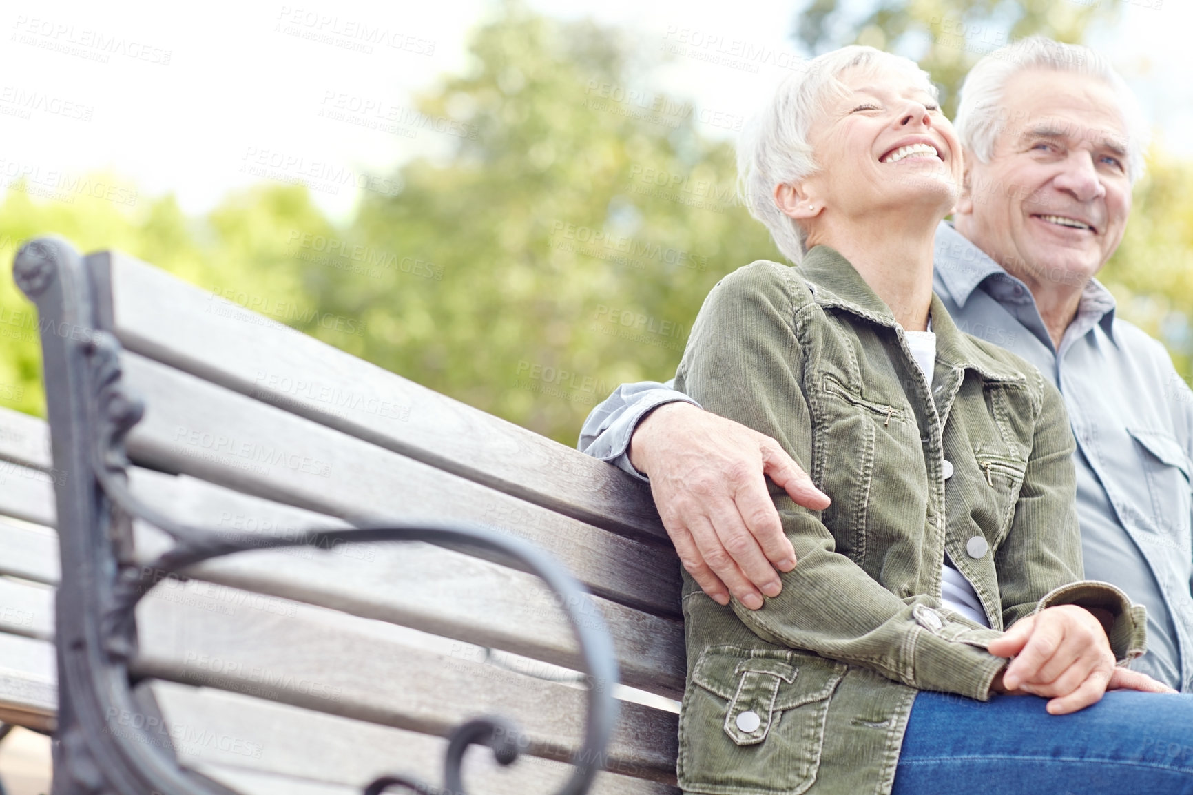 Buy stock photo A mature couple sitting on a bench in the park and laughing together