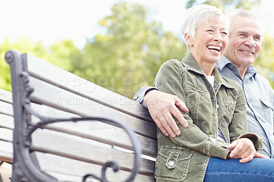 Buy stock photo A mature couple sitting on a bench in the park and laughing together