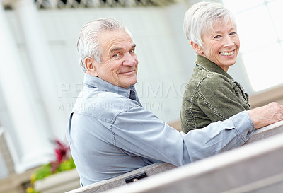 Buy stock photo Portrait of a mature couple sitting on a bench together and smiling at the camera