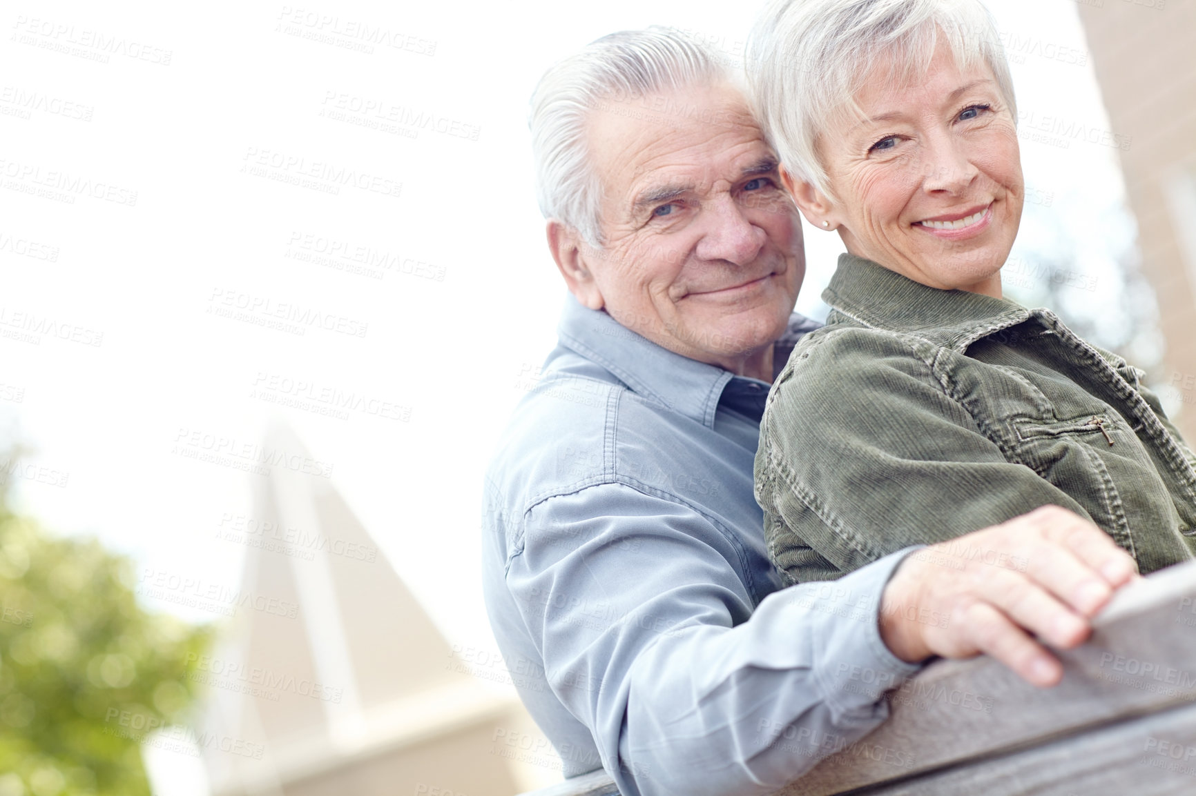 Buy stock photo Portrait of a mature couple sitting on a bench together and smiling at the camera