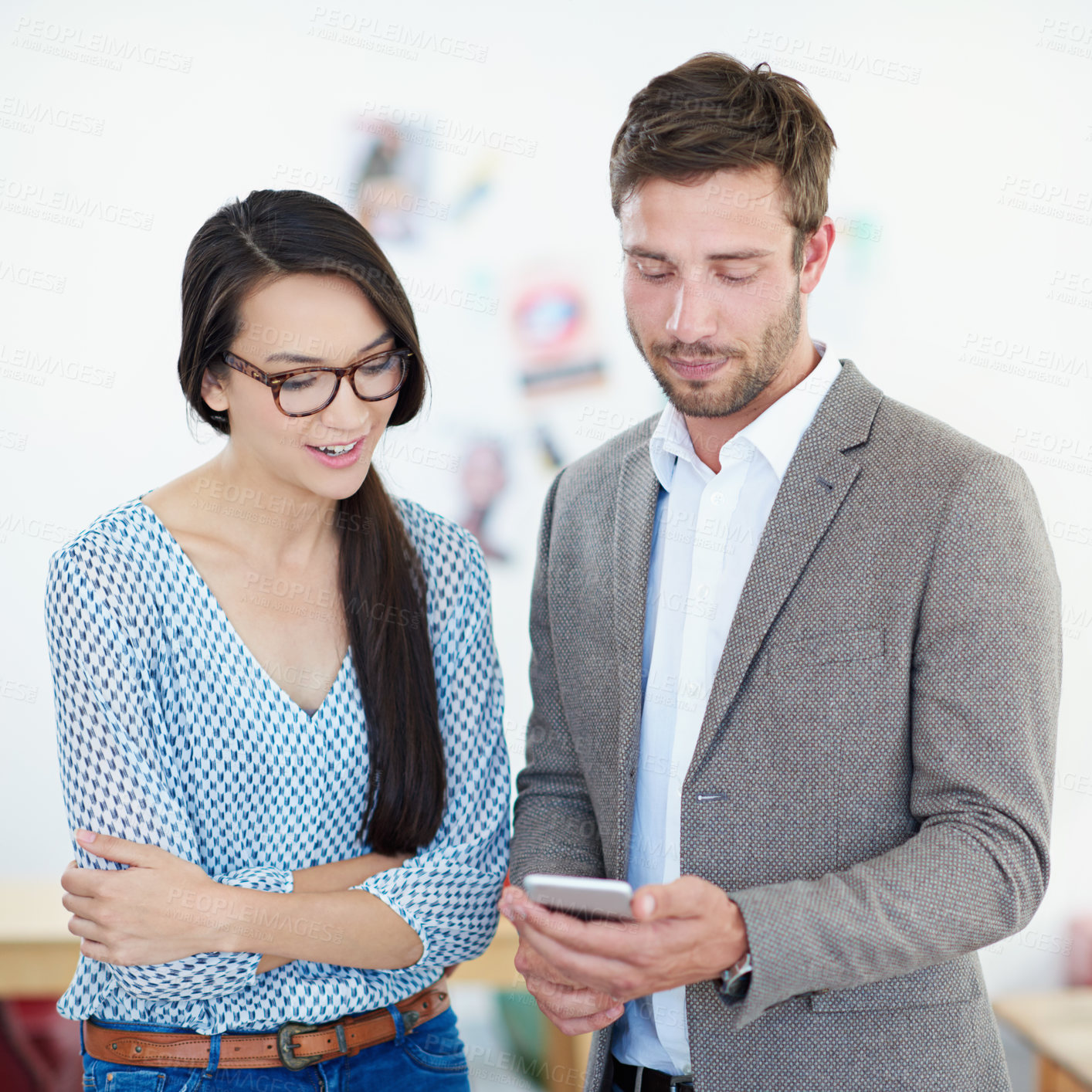 Buy stock photo Shot of two coworkers looking at a cellphone while standing in their office