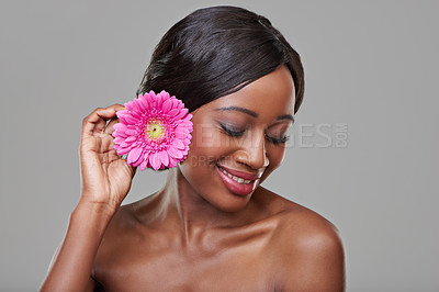 Buy stock photo Woman, skincare and happy with flower in studio for beauty, organic cosmetics and makeup by grey background. Girl, model and African person with pink daisy, thinking and ecology with natural glow