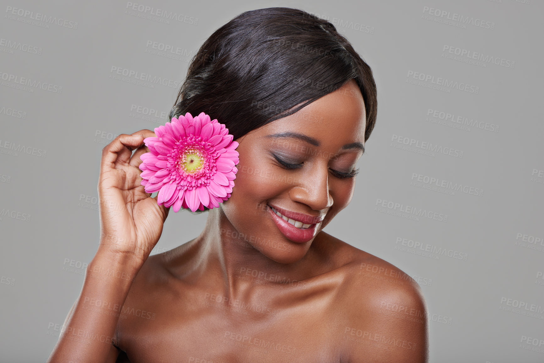 Buy stock photo Woman, skincare and happy with flower in studio for beauty, organic cosmetics and makeup by grey background. Girl, model and African person with pink daisy, thinking and ecology with natural glow