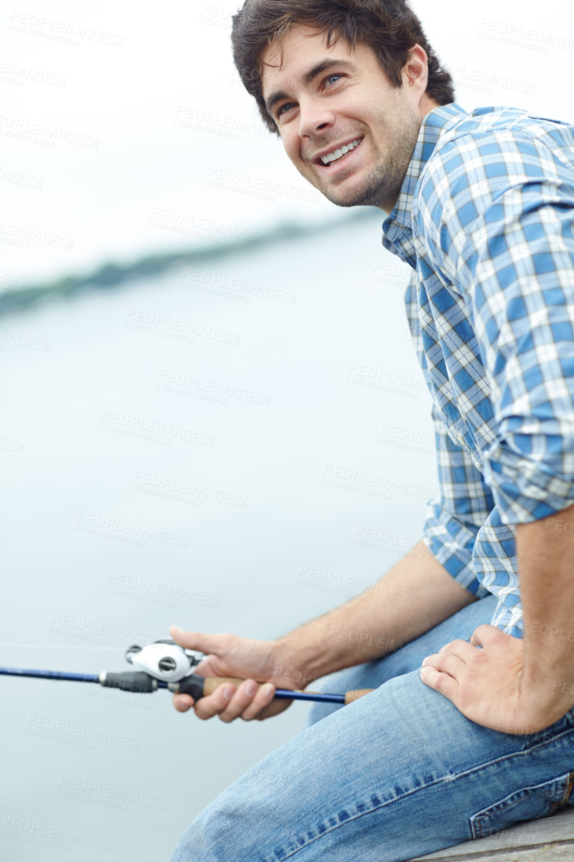 Buy stock photo A young guy sitting on the jetty and doing some fishing