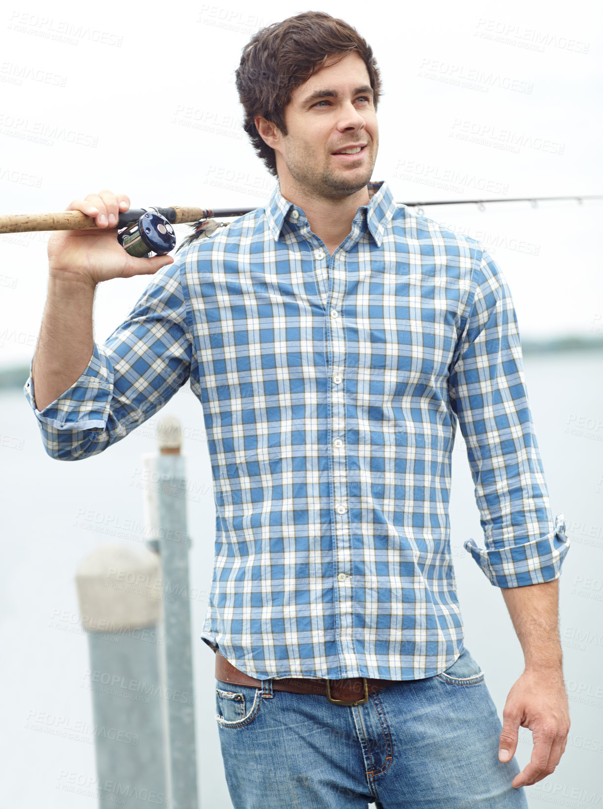 Buy stock photo A handsome young fisherman standing at the lake while carrying his gear