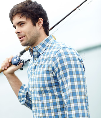 Buy stock photo A handsome young fisherman standing at the lake while carrying his gear